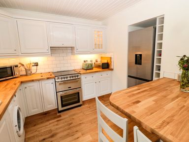 A kitchen with white cabinets wooden countertops a stainless steel oven and refrigerator at Curlew Cottage 2 Fenkle Street Holy Island