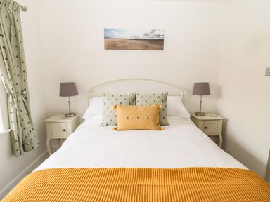 A bedroom with a white bed having yellow blanket and decorative pillows with two bedside tables and lamps at Curlew Cottage 2 Fenkle Street Holy Island