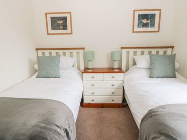 A bedroom with two single beds with pillows a bedside table with lamps and framed bird pictures on the wall at Curlew Cottage 2 Fenkle Street Holy Island