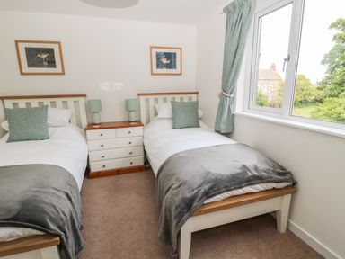 A bedroom with two single beds a window a nightstand with two lamps and framed pictures on the wall at Curlew Cottage 2 Fenkle Street Holy Island
