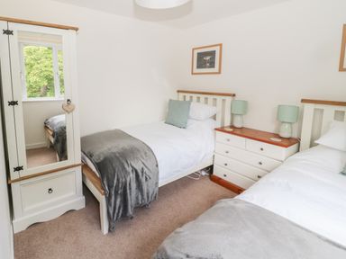 A bedroom with two single beds a wardrobe with mirror and a chest of drawers with table lamps at Curlew Cottage 2 Fenkle Street Holy Island