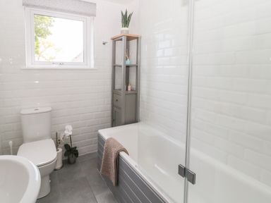 A bathroom with a toilet sink bathtub and a shelf with a plant at Curlew Cottage 2 Fenkle Street Holy Island