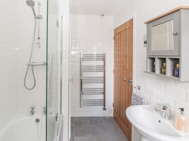 A bathroom with a shower bathtub towel rack wooden door and a sink with a wall cabinet at Curlew Cottage 2 Fenkle Street Holy Island