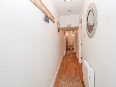 A hallway with wooden floor a round wall mirror coat hooks and a door leading to a bathroom at Curlew Cottage 2 Fenkle Street Holy Island