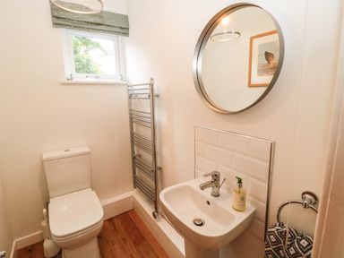 A small bathroom with a toilet, a sink with soap, a round mirror, a towel rail, and a window at Curlew Cottage 2 Fenkle Street Holy Island