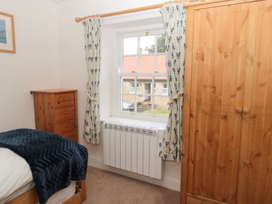 A bedroom with a wooden wardrobe a chest of drawers a bed with a blanket and a window with curtains at Curlew Cottage 2 Fenkle Street Holy Island