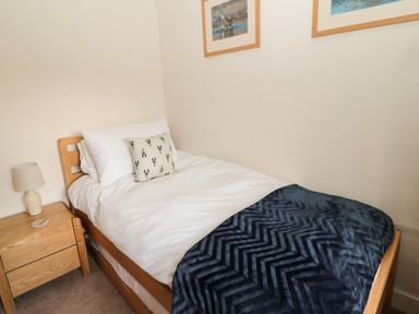 A single bed with white bedding and a dark blue blanket next to a wooden nightstand with a lamp at Curlew Cottage 2 Fenkle Street Holy Island