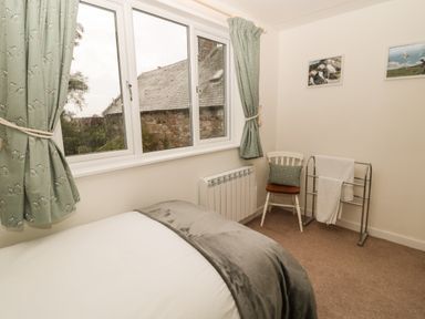 A bedroom with a bed a window with curtains a chair with a cushion and a towel rack at Curlew Cottage 2 Fenkle Street Holy Island