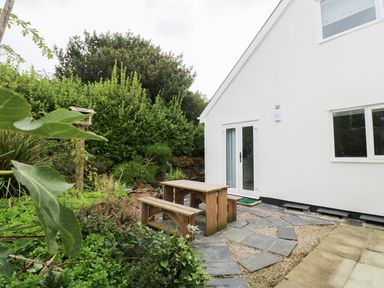 A garden area with a wooden picnic table and benches outside a white house at Alice Cottage Wheal Kitty near St Agnes