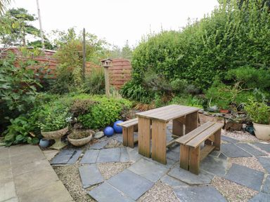 A garden area with a wooden picnic table and benches surrounded by plants and a wooden fence at Alice Cottage in Wheal Kitty near St Agnes