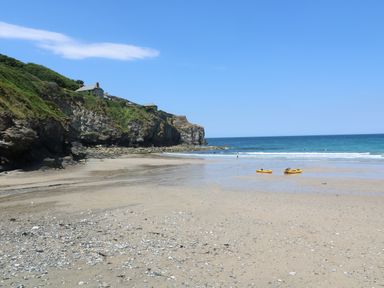 A sandy beach with two yellow kayaks near the water and houses on a rocky cliff at Alice Cottage in Wheal Kitty near St Agnes
