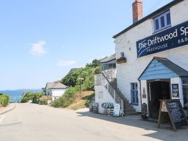 A road beside a white building with a sign The Driftwood Spars near the sea