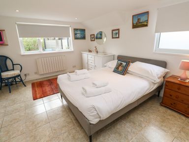 A bedroom with a bed and folded towels on it a wooden chest of drawers with a lamp and a white dresser with a mirror at Alice Cottage in Wheal Kitty near St Agnes