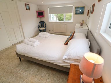 A bedroom with a double bed and towels on it a bedside table with a lamp a chair a small television and framed pictures on the walls at Alice Cottage in Wheal Kitty near St Agnes