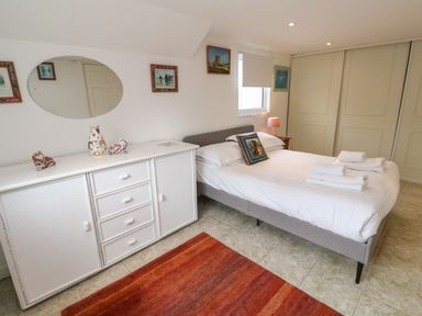A bedroom with a bed with folded towels bedside table with lamp large wardrobe and white dresser with decorative items at Alice Cottage Wheal Kitty near St Agnes