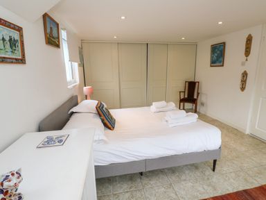 A bedroom with a bed and folded towels a dresser with a ceramic cat a chair and paintings on walls at Alice Cottage Wheal Kitty near St Agnes