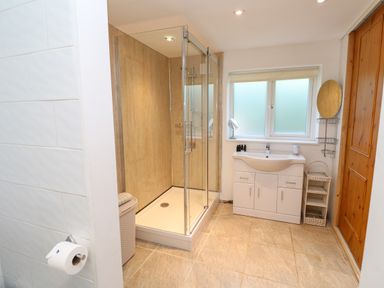 A bathroom with a glass shower enclosure a white sink cabinet a window and a wooden door at Alice Cottage in Wheal Kitty near St Agnes