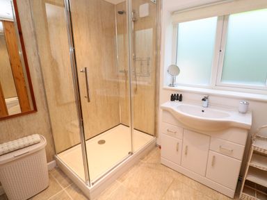 A bathroom with a glass shower enclosure a white sink vanity a window and a wicker laundry basket at Alice Cottage in Wheal Kitty near St Agnes