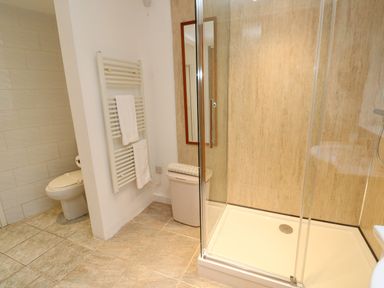 A bathroom with a shower enclosure towel rack with towels a toilet and a laundry basket at Alice Cottage in Wheal Kitty near St Agnes