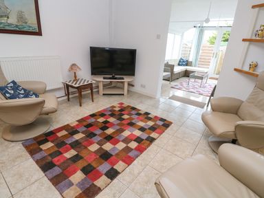 A living room with two beige chairs a multicolored checkered rug a small table with a lamp and a television at Alice Cottage in Wheal Kitty near St Agnes