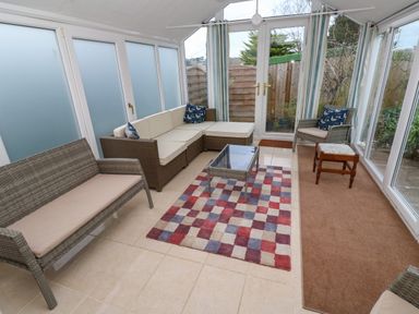 A sunroom with wicker sofas a glass coffee table and a checkered rug at Alice Cottage in Wheal Kitty near St Agnes