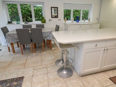 A dining area with a table covered by a patterned cloth and six chairs next to a kitchen island with two bar stools at Alice Cottage Wheal Kitty near St Agnes