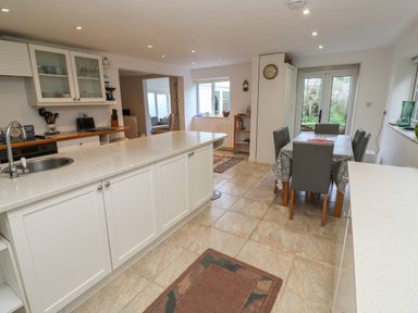 A kitchen with a large island, dining table with chairs, and a view of a garden through glass doors at Alice Cottage in Wheal Kitty near St Agnes