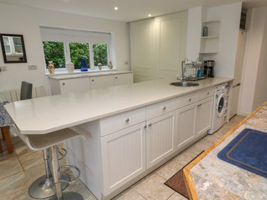 A kitchen with a countertop island with a sink and bar stools and a washing machine at Alice Cottage in Wheal Kitty near St Agnes