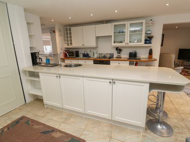 A kitchen with white cabinets a countertop sink bar stools and appliances at Alice Cottage in Wheal Kitty near St Agnes