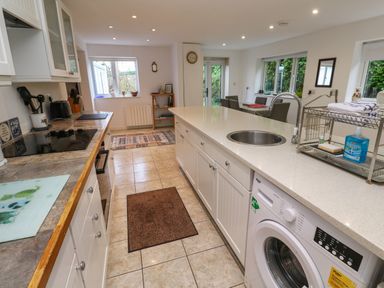A kitchen with white cabinets countertops a washing machine a stove and a dining table at Alice Cottage in Wheal Kitty near St Agnes
