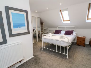 A bedroom with a white metal bed frame two skylight windows and wooden furniture at Alice Cottage in Wheal Kitty near St Agnes