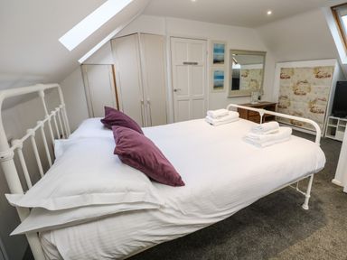 A bedroom with a bed with white sheets and purple pillows a wardrobe a mirror and a television at Alice Cottage in Wheal Kitty near St Agnes
