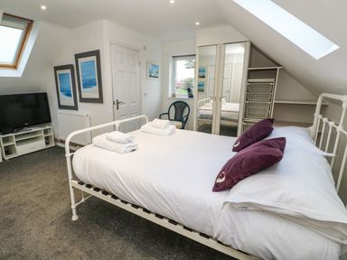 A bedroom with a white bed and purple pillows a TV on a stand and mirrored wardrobes at Alice Cottage in Wheal Kitty near St Agnes