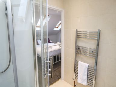 A bathroom with a glass shower enclosure and a chrome towel radiator with a white towel at Alice Cottage in Wheal Kitty near St Agnes