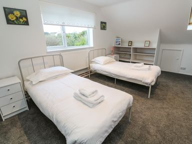 A bedroom with two single beds with white bedding and folded towels a window with a blind small bedside tables and wall art at Alice Cottage Wheal Kitty near St Agnes