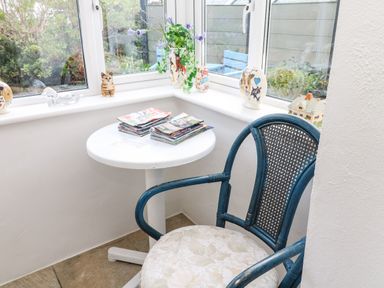 A corner with a round white table holding magazines and a blue woven chair at Alice Cottage in Wheal Kitty near St Agnes