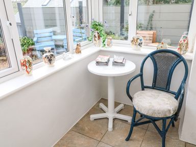 A corner with windows a white round table with magazines a blue chair and decorative vases on the windowsill at Alice Cottage Wheal Kitty near St Agnes