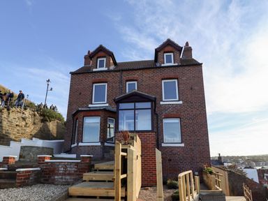 A brick house with multiple windows and wooden stairs leading up to the entrance at Mariners Watch in Whitby