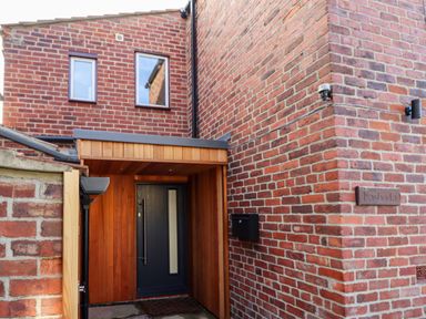 An entrance with a black door and wooden cladding surrounded by brick walls at Mariner's Watch in Whitby