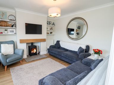 A living room with two blue sofas a blue armchair a fireplace with fire a wall-mounted TV and shelves with decorations at Mariners Watch in Whitby