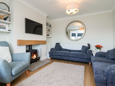 A living room with blue sofas a chair a fireplace and a round mirror at Mariners Watch in Whitby