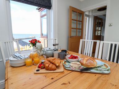 A dining table set with plates knives glasses of orange juice croissants bread strawberries and tea set near a window with a sea view at Mariners Watch in Whitby