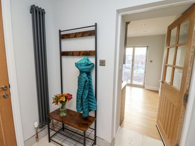 A hallway with a wooden coat rack holding a blue jacket and a vase of flowers beside an open wooden door at Mariners Watch in Whitby