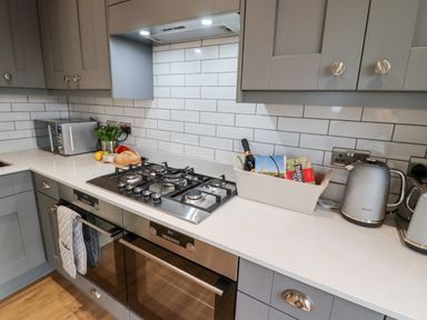 A kitchen countertop with a gas stove oven microwave kettle toaster and a basket with bottles and brochures at Mariners Watch in Whitby