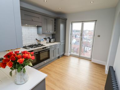 A kitchen with grey cabinets a gas stove an oven and a vase of orange roses on the counter at Mariners Watch in Whitby