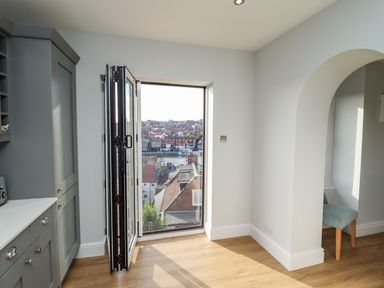 A kitchen area with gray cabinets and bi-fold doors opening to a view of a town at Mariners Watch in Whitby