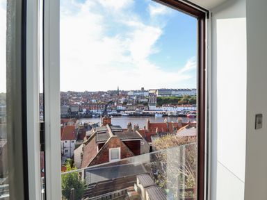 A view through a window showing rooftops and a river with buildings on the opposite side at Mariners Watch in Whitby