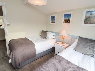A bedroom with two single beds with grey pillows and throws a bedside table and lamp and three framed pictures on the wall at Mariners Watch in Whitby