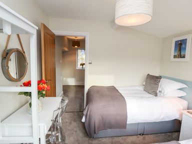 A bedroom with a bed a desk with flowers a mirror and a doorway at Mariners Watch in Whitby
