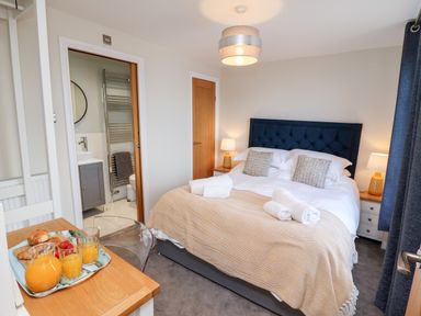 A bedroom with a bed with pillows and a blanket and towels on it and a tray with orange juice and croissants at Mariners Watch in Whitby
